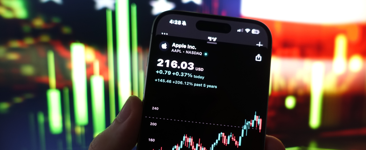 hand holding a phone showing a trading app with Apple stock price